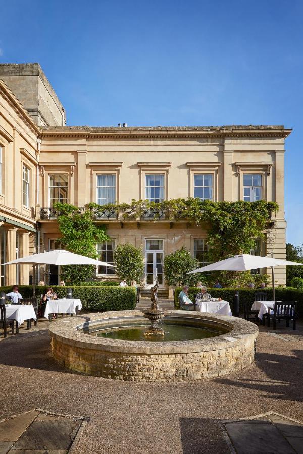 Macdonald Bath Spa Hotel Екстериор снимка The photo depicts a charming outdoor dining area of a classic-looking building with elegant architecture. The structure features large windows and is adorned with greenery, including climbing plants. In the foreground, there is a circular fountain, a