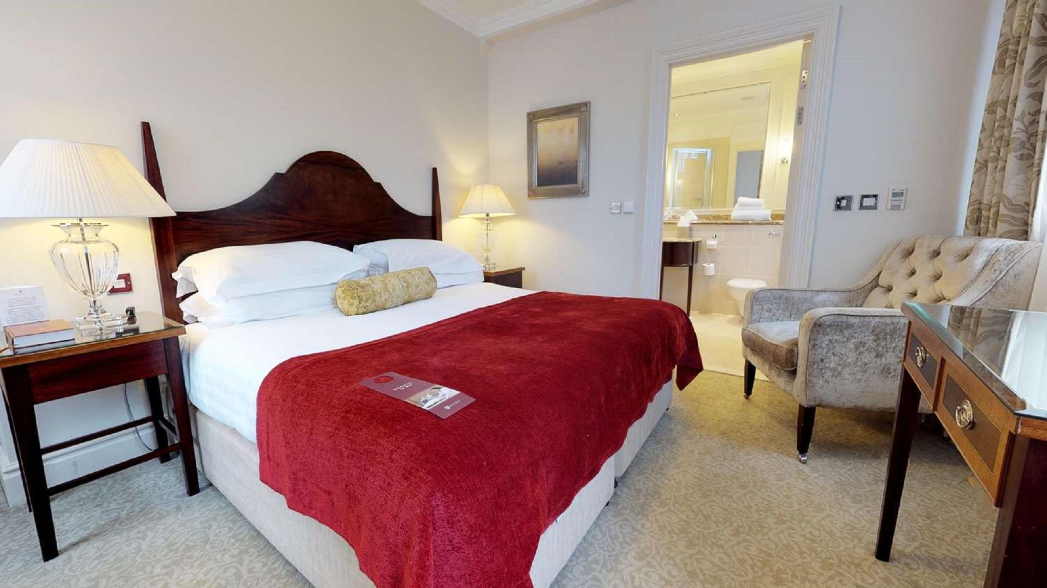 Macdonald Bath Spa Hotel Екстериор снимка The photo shows a well-furnished hotel room. In the center, there is a large bed with white linens and a red throw blanket. A decorative pillow is placed on the bed. On either side of the bed, there are bedside tables with lamps. To the right, there 