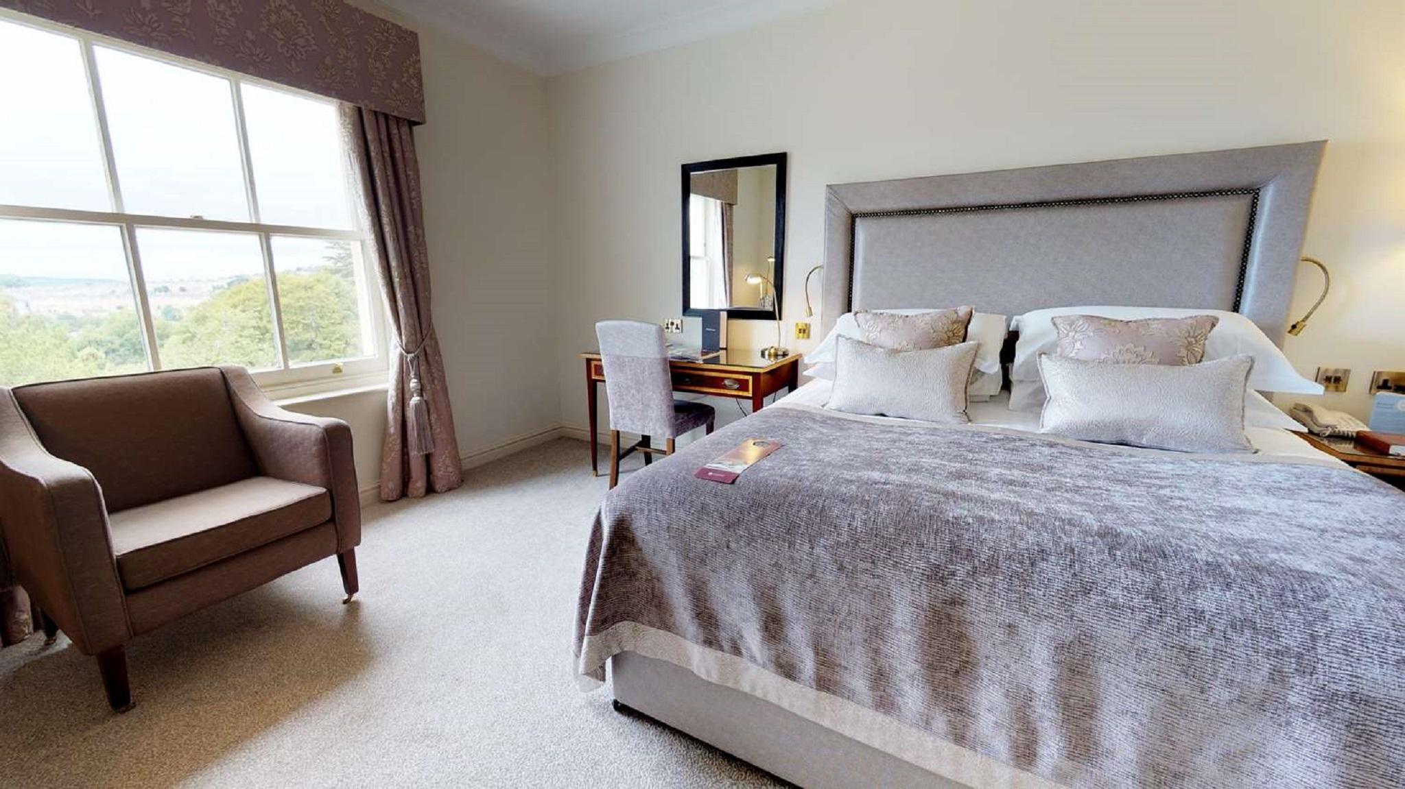 Macdonald Bath Spa Hotel Екстериор снимка The photo shows a cozy and well-decorated bedroom. It features a large bed with a plush, grey bedspread and several decorative pillows. Beside the bed, there is a wooden bedside table with a lamp. A small desk and chair are positioned near a window, 