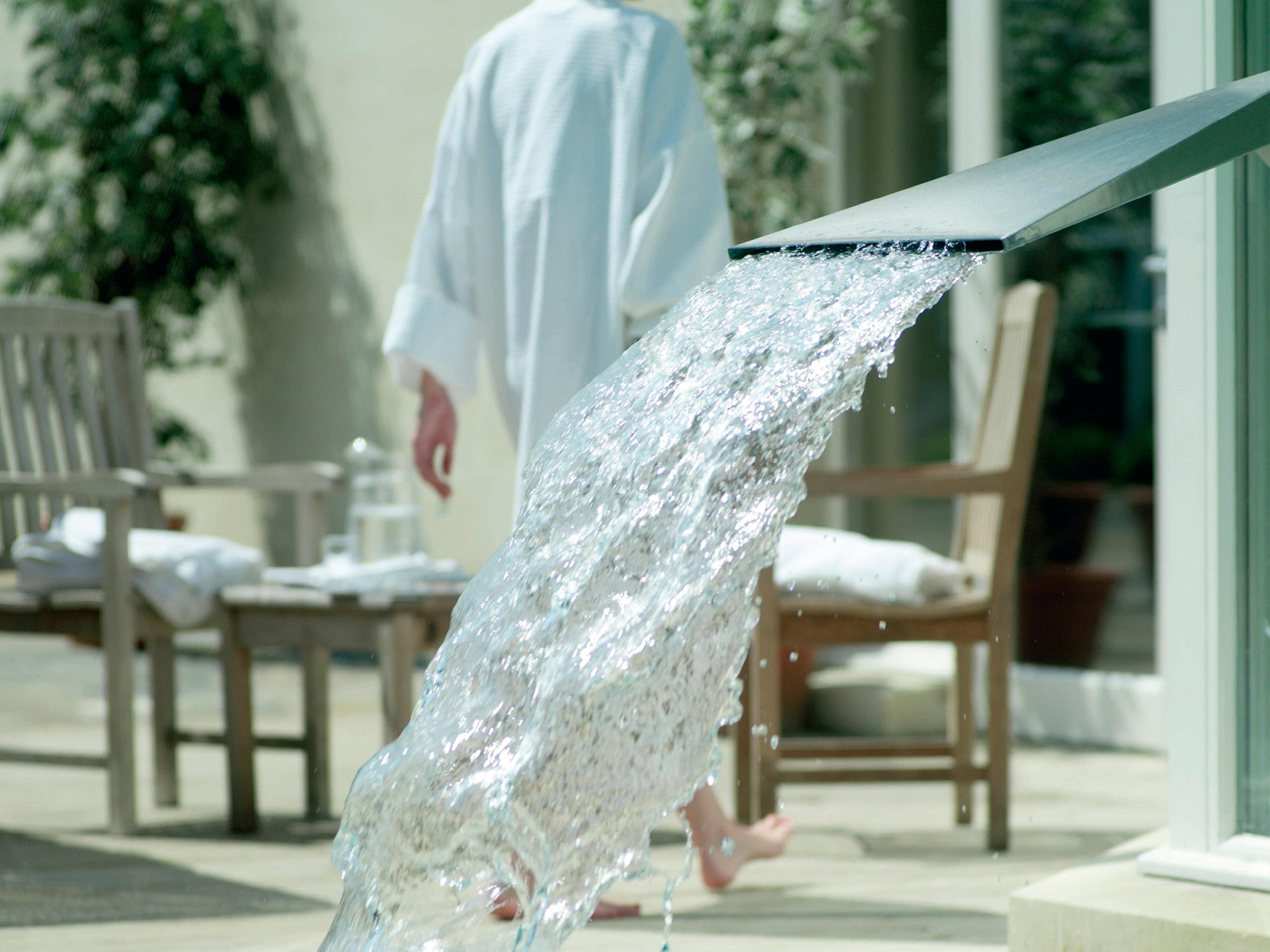 Macdonald Bath Spa Hotel Екстериор снимка The photo shows a flowing water feature, with water elegantly cascading from a sleek spout. In the background, there is a person wearing a white bathrobe, walking away. Surrounding the area, there are wooden chairs and what appears to be a serene out