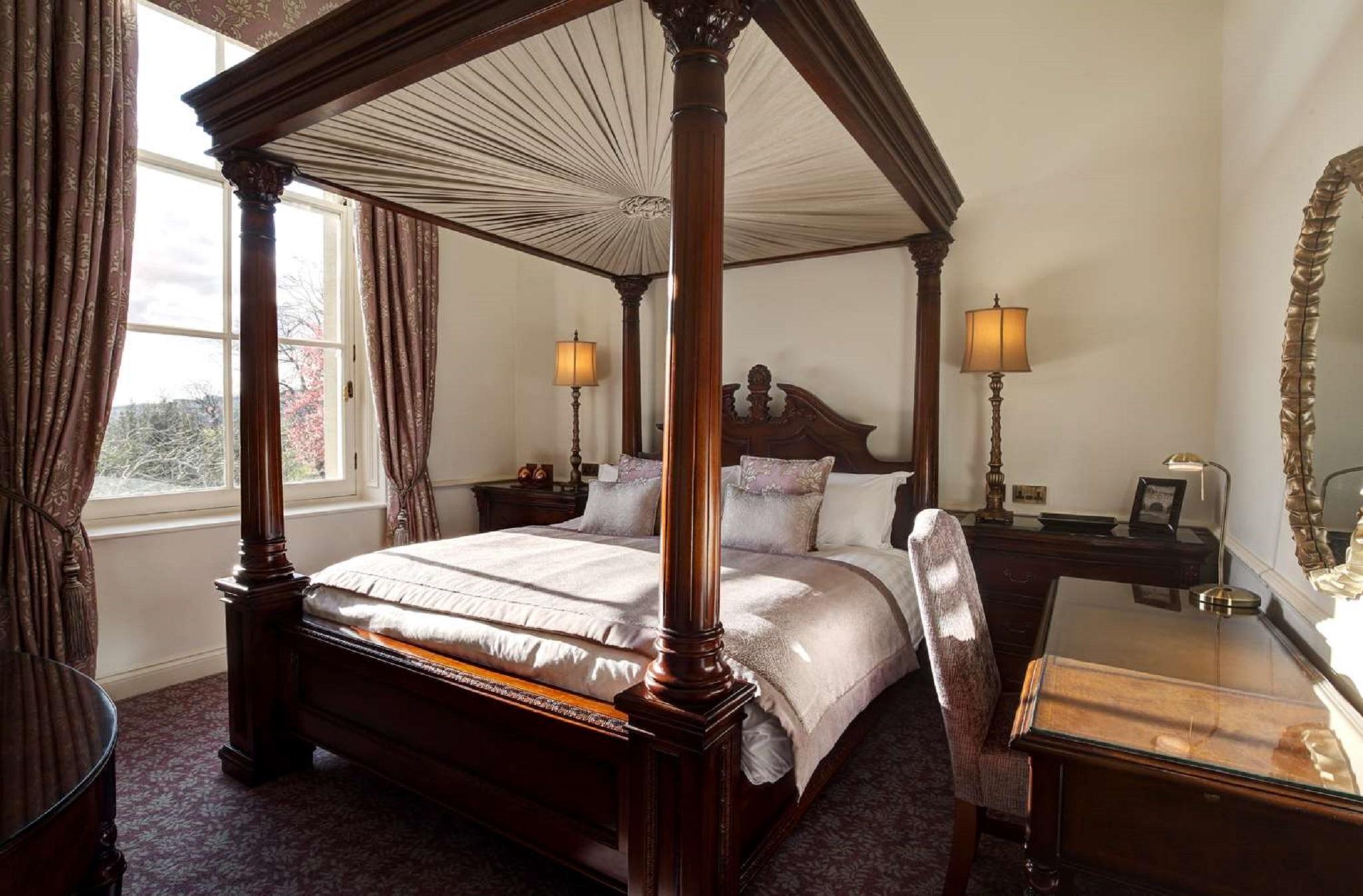 Macdonald Bath Spa Hotel Екстериор снимка The photo shows a well-decorated bedroom featuring a four-poster bed with an elegant wooden frame. The bed is dressed with light-colored linens and several decorative pillows. On either side of the bed, there are matching bedside lamps that provide s