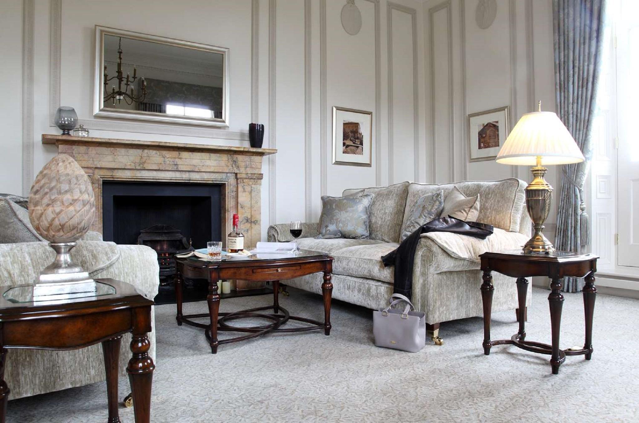 Macdonald Bath Spa Hotel Екстериор снимка The photo shows a stylish living room. It features a plush light-colored sofa adorned with decorative pillows. Next to the sofa, there is a small wooden coffee table with a decorative item and a bottle of wine, along with a glass. A larger wooden tab