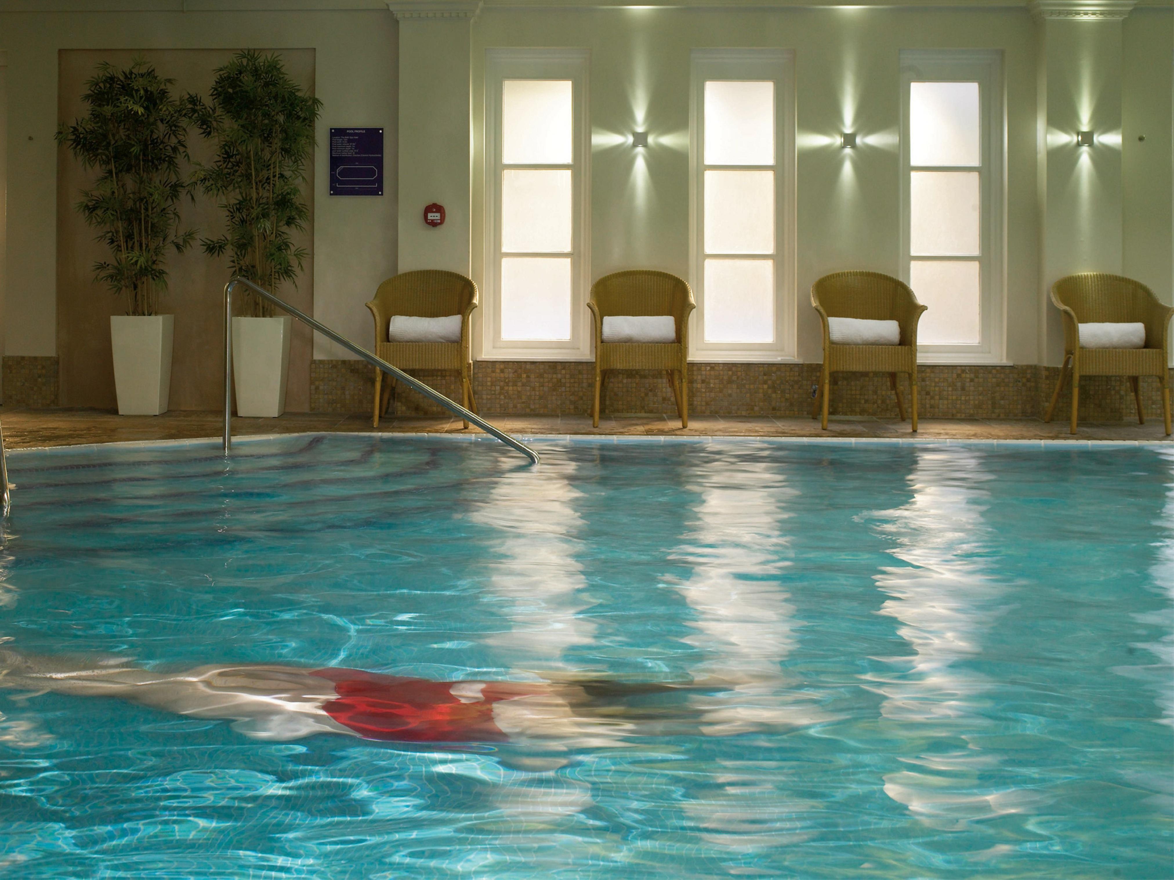 Macdonald Bath Spa Hotel Екстериор снимка The photo shows an indoor swimming pool with clear, blue water. In the pool, a person is swimming, partially submerged, and wearing a red swimsuit. Surrounding the pool, there are several empty chairs arranged along the side, along with potted plants