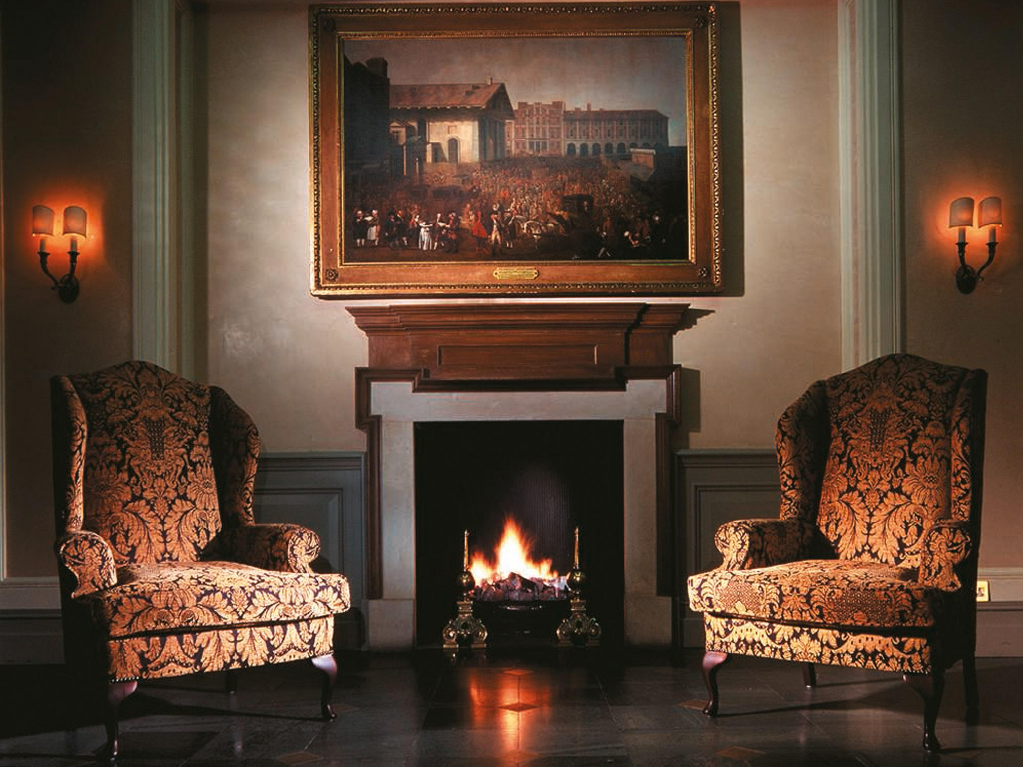 Macdonald Bath Spa Hotel Екстериор снимка The image shows a cozy indoor setting featuring two ornate armchairs placed opposite a fireplace. Above the fireplace hangs a large painting in a decorative frame. The warm glow from the fire illuminates the room, and there are wall sconces providing