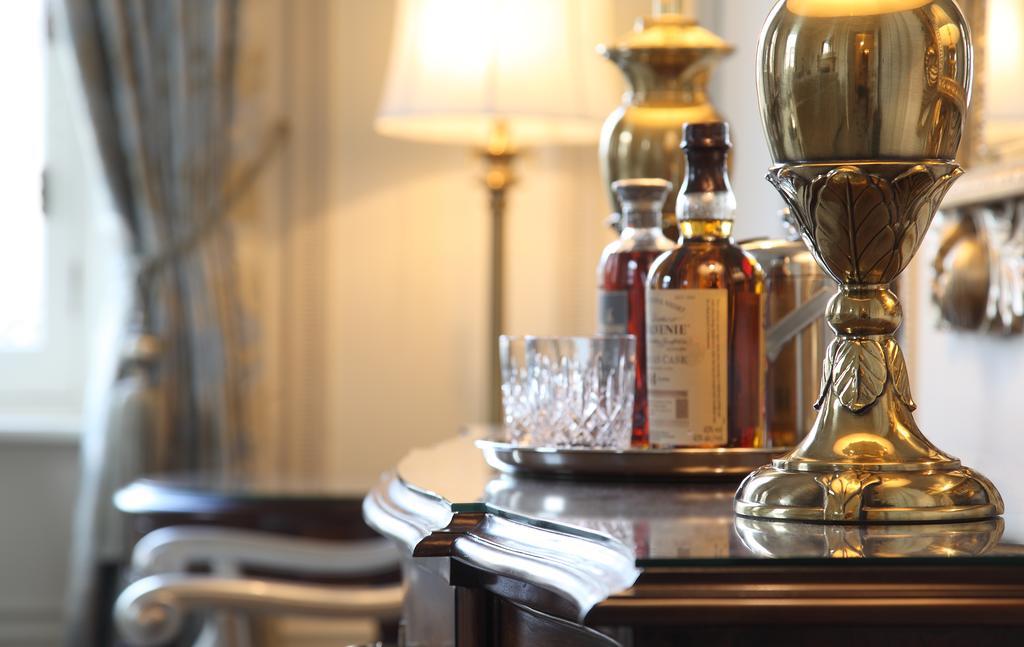 Macdonald Bath Spa Hotel Екстериор снимка The photo features an elegant interior scene that includes a polished wooden bar or table. On the surface, there are several bottles of liquor, likely whiskey, each with a distinctive label. A glass, possibly for drinking, is positioned near the bott