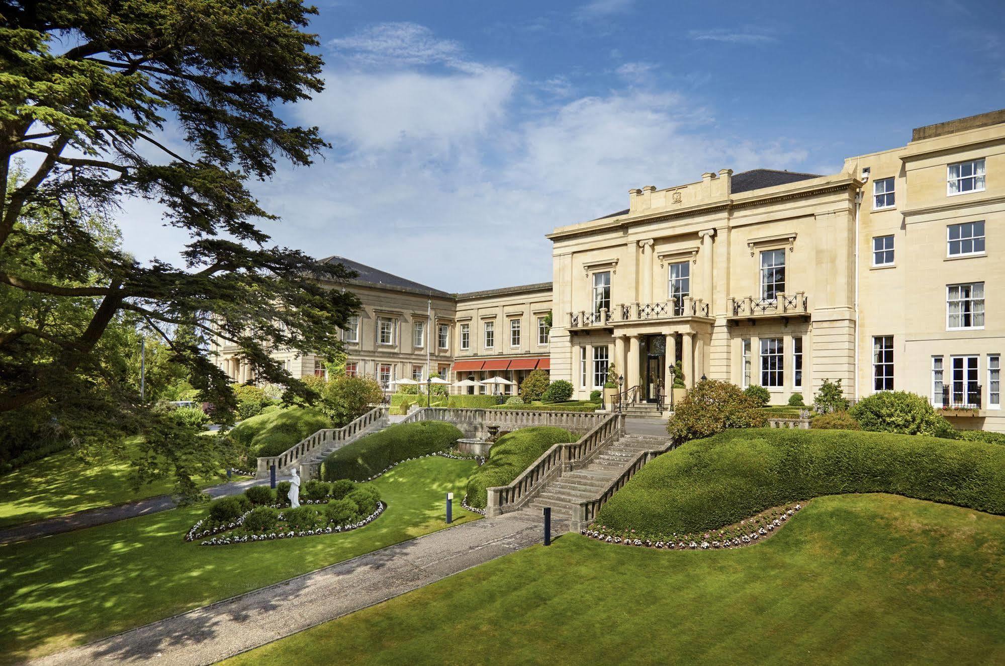 Macdonald Bath Spa Hotel Екстериор снимка The photo shows a grand building, likely a hotel or estate, surrounded by well-manicured gardens and lawns. The architecture appears elegant, with multiple stories and large windows. There are steps leading up to the entrance, and the setting include